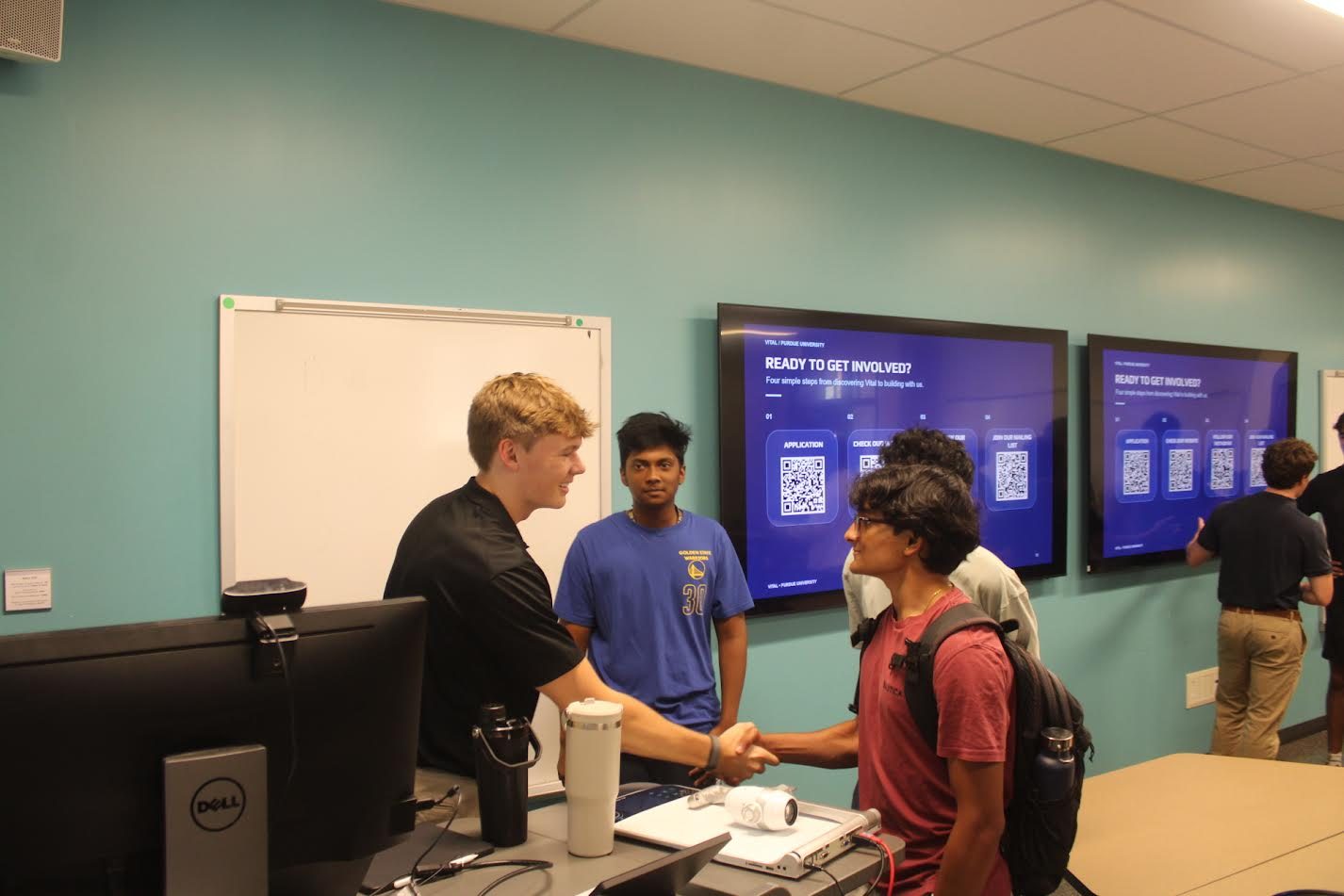 An exec board member shaking hands with a student after the callout, in front of screens showing how to get involved
